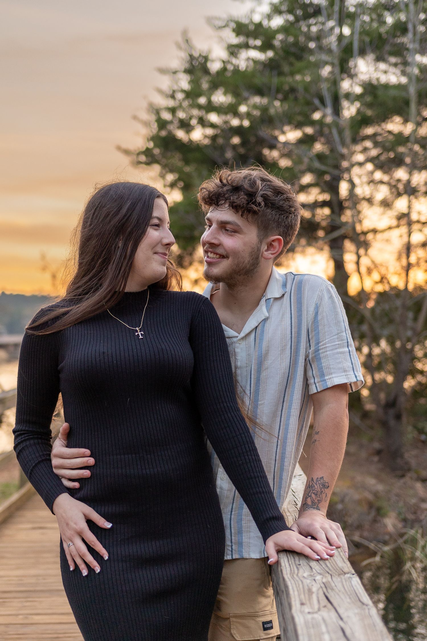 A couple shares an intimate moment on a boardwalk during sunset.