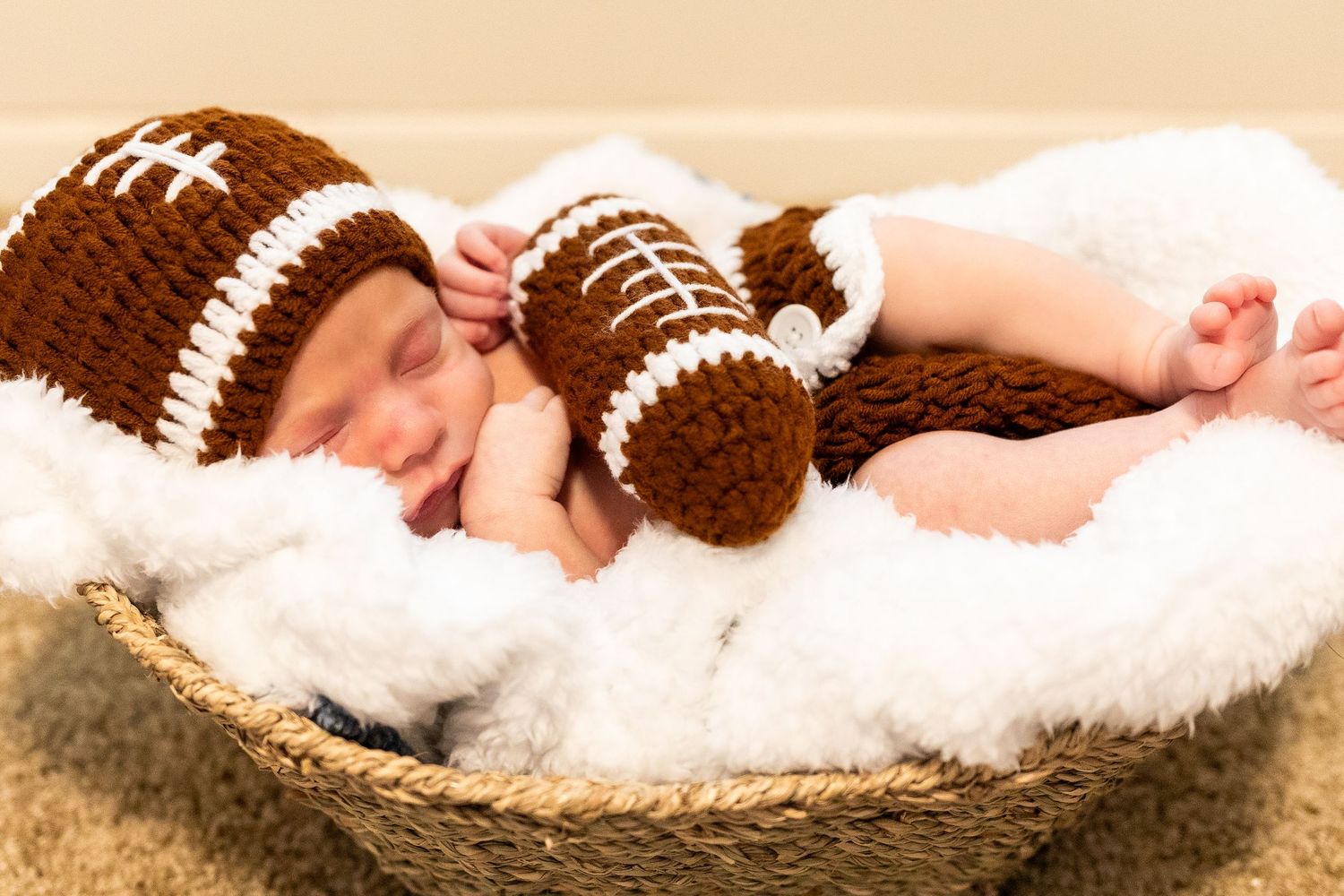 Newborn photography setup with brown football-themed props on soft white blankets.