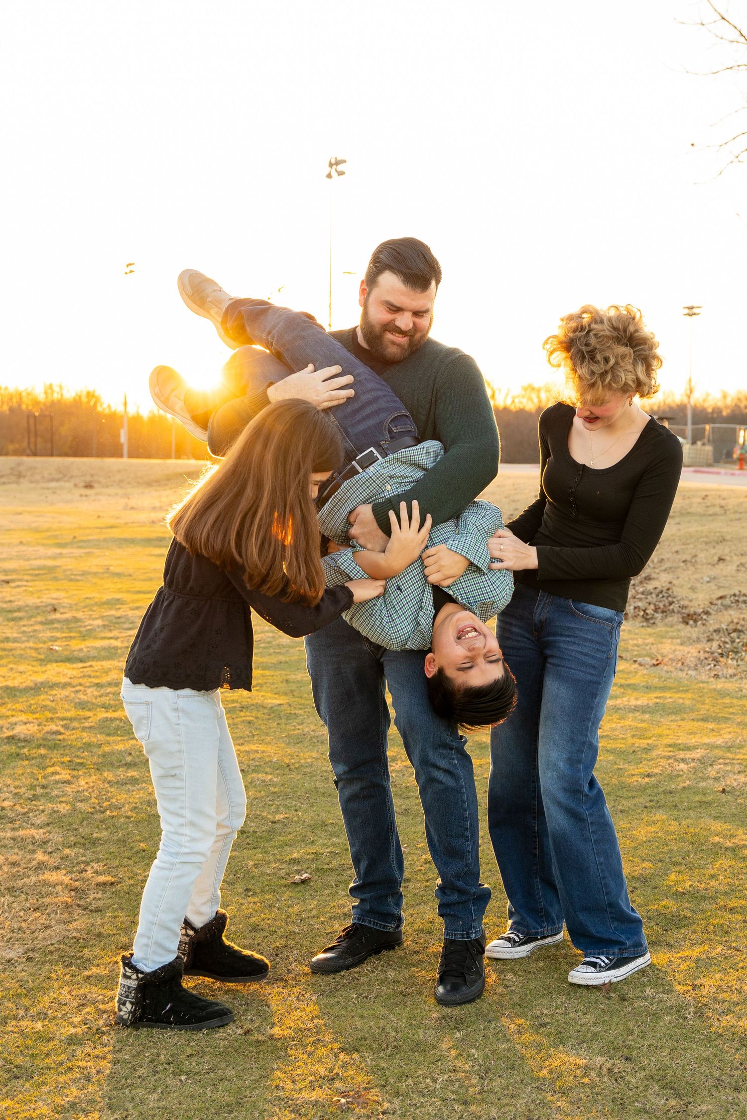 Playful family moment captured in a field at sunset with dynamic poses and movement.