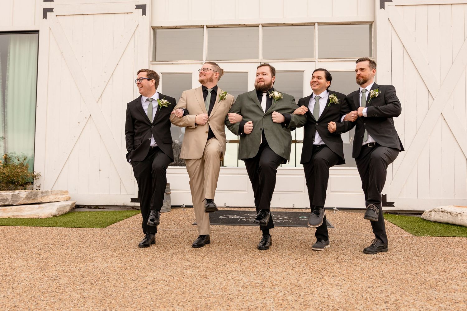 Groomsmen in suits running playfully down a pathway.