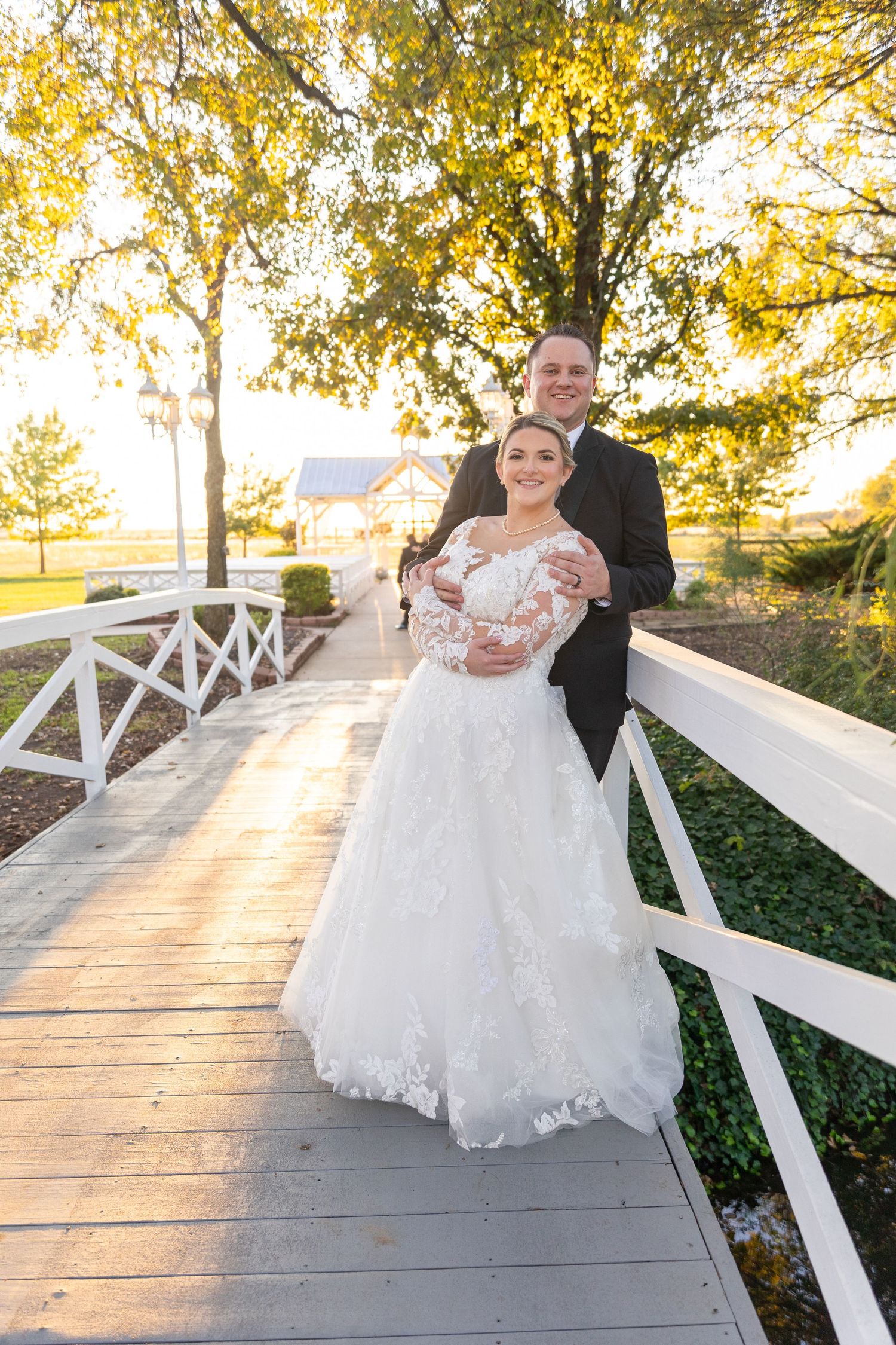 Wedding couple posing on white wooden bridge during golden hour.