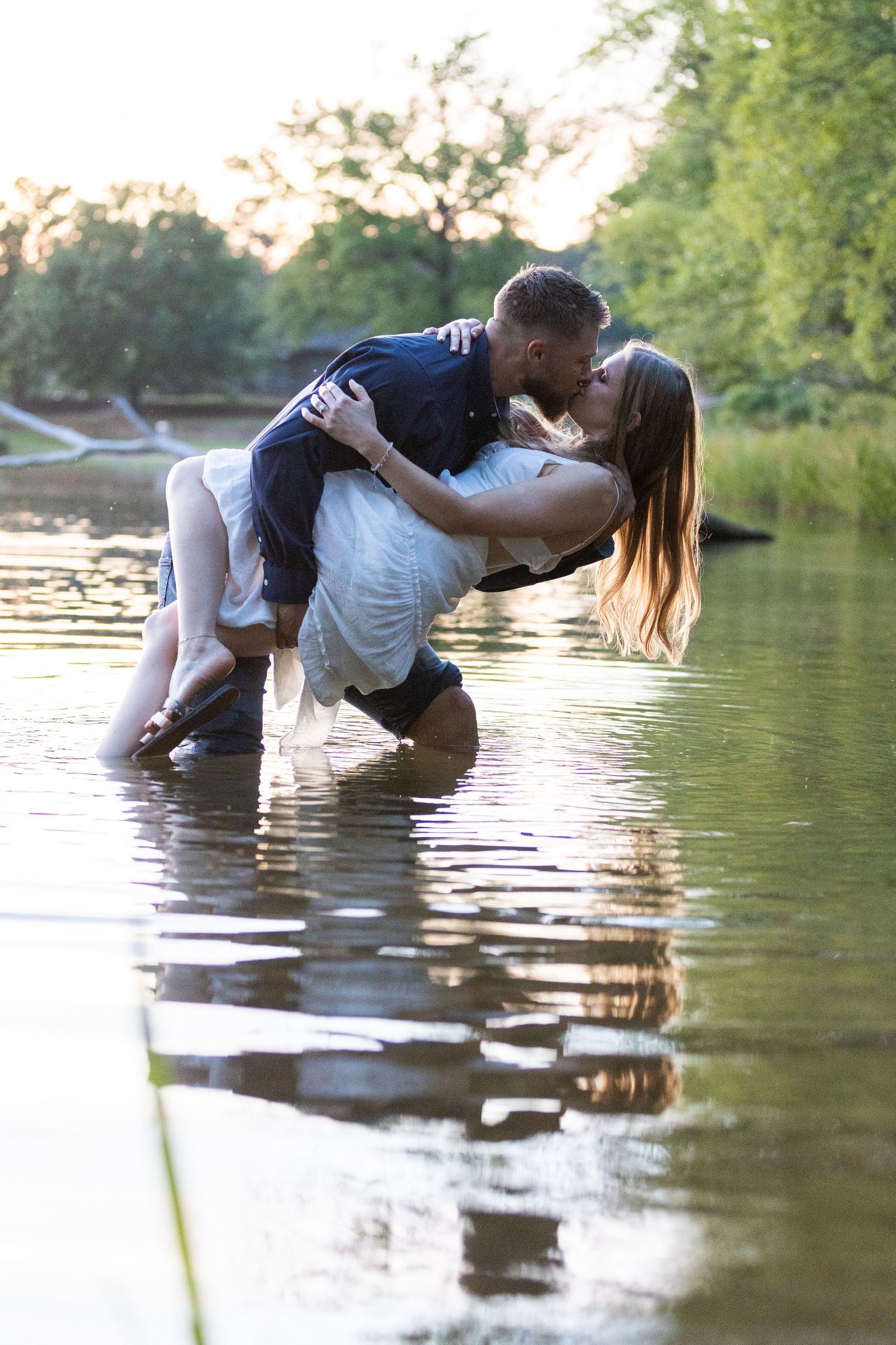 Couple creates romantic pose while wading in reflective lake water.