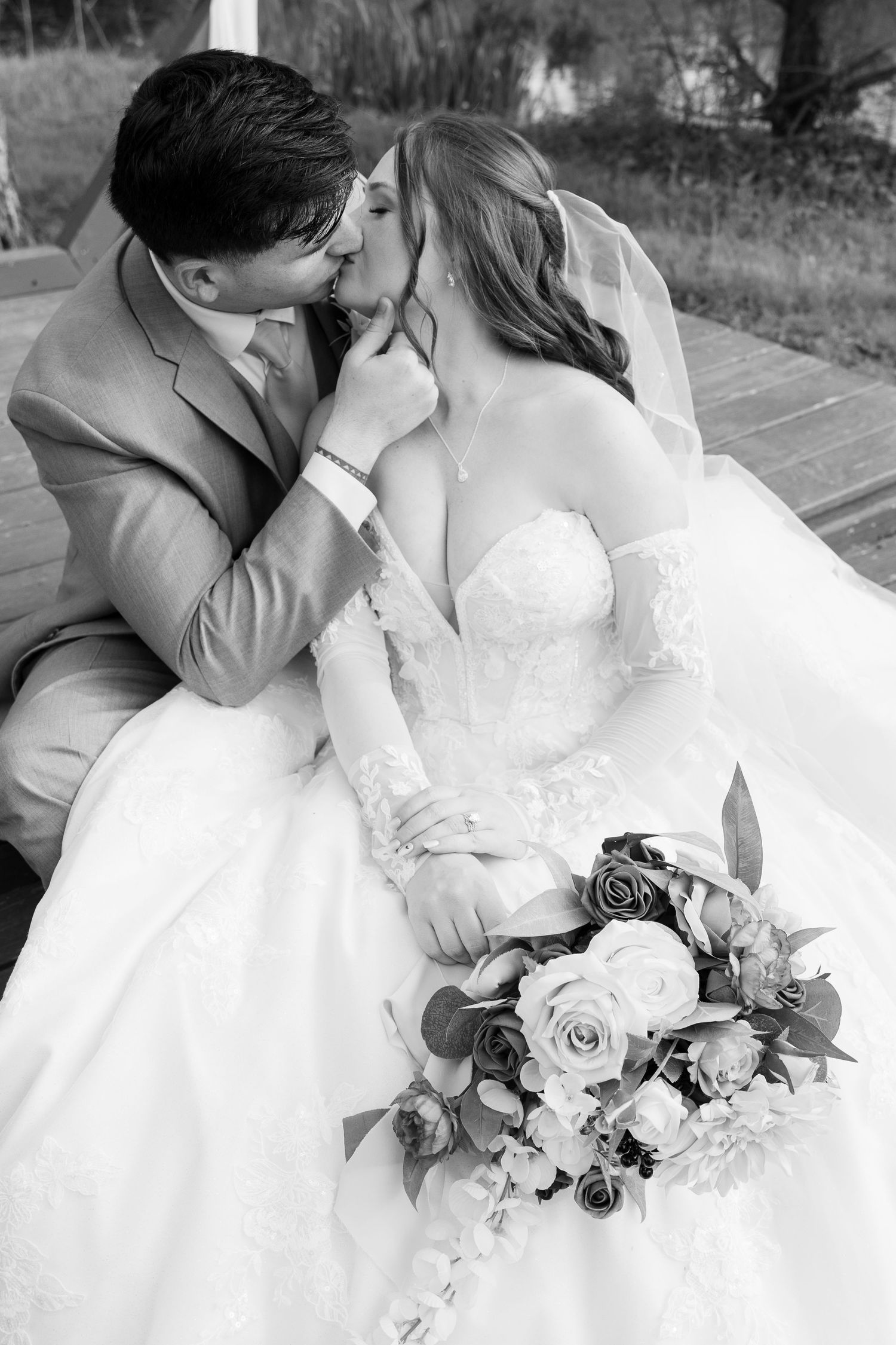 A black and white wedding photo showing an intimate moment with a bridal bouquet of roses.