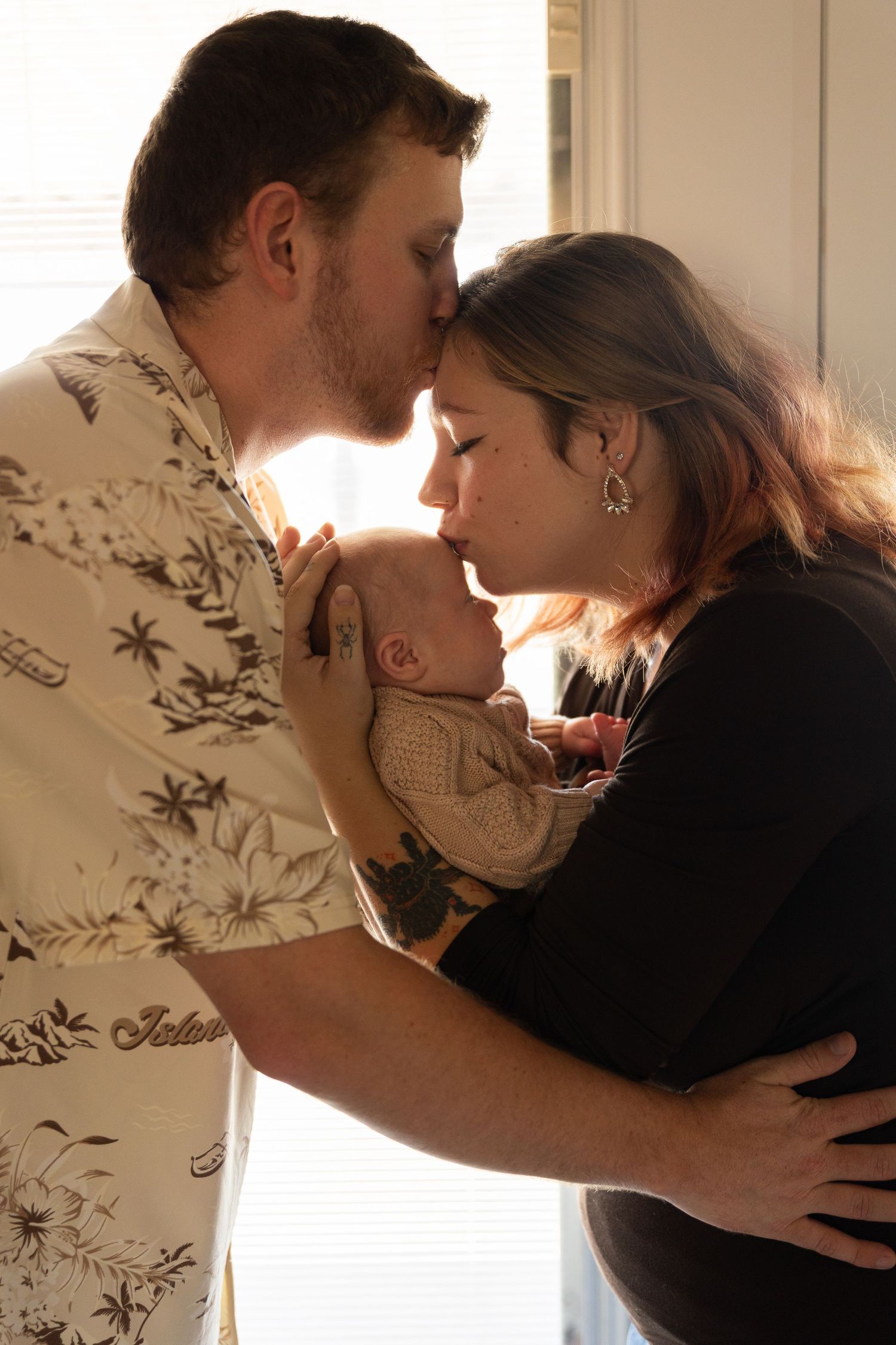 Intimate family moment with newborn baby in soft window lighting.