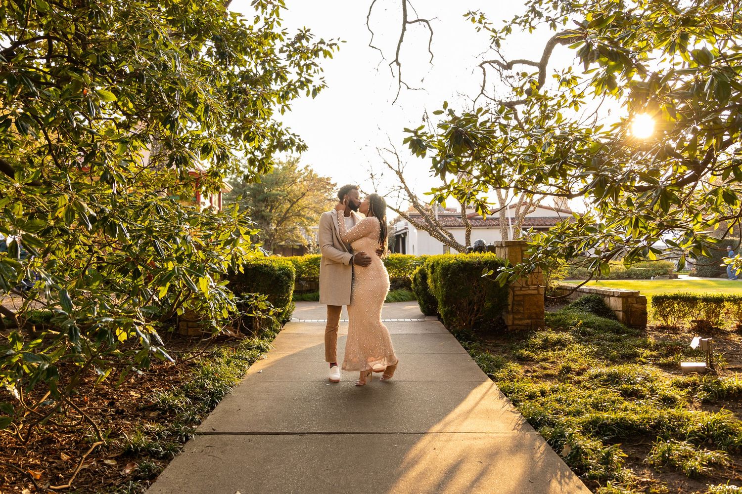 A couple sharing a romantic moment on a garden path during sunset.