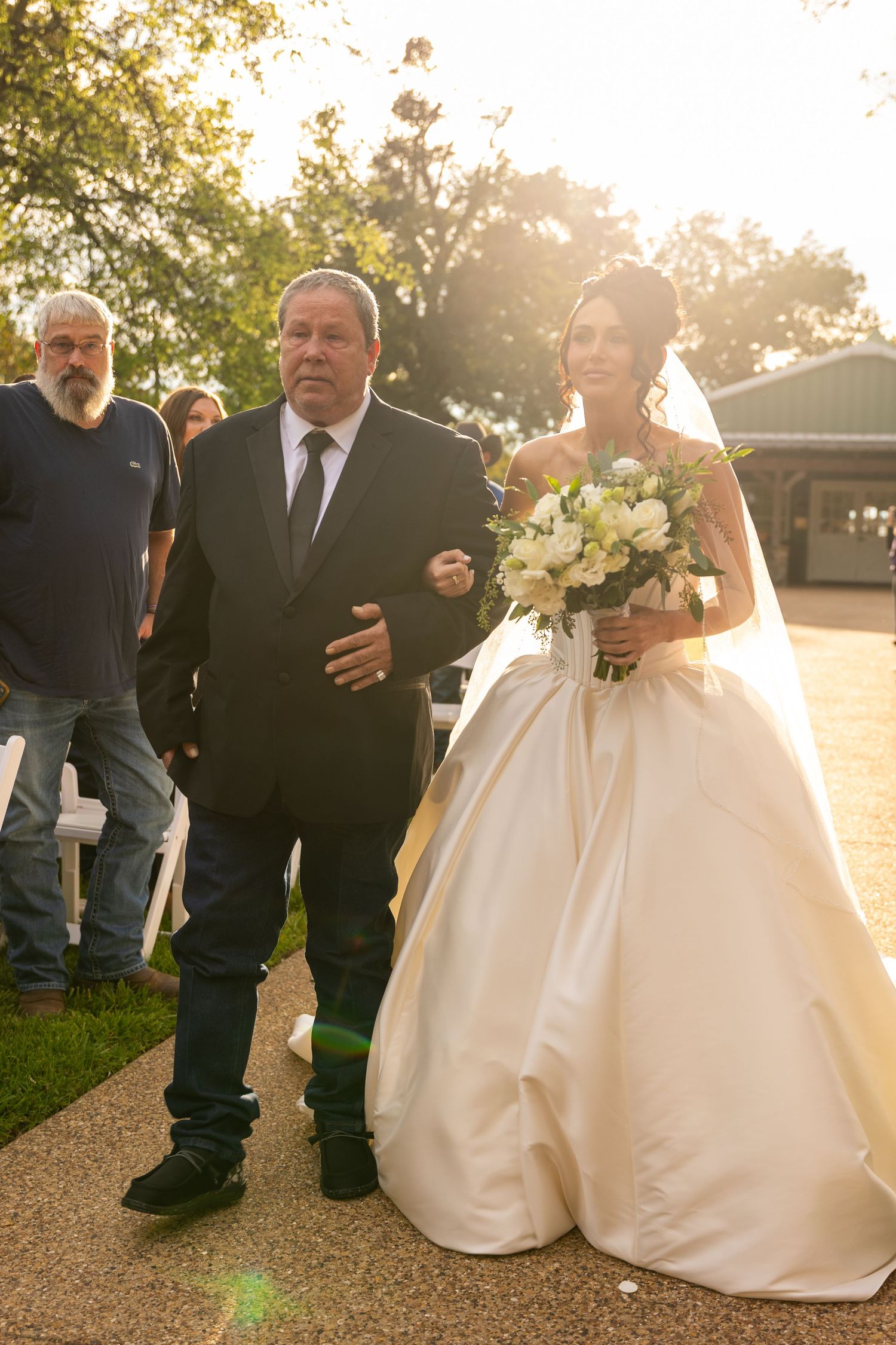 Wedding ceremony processional on stone pathway with white floral arrangements.