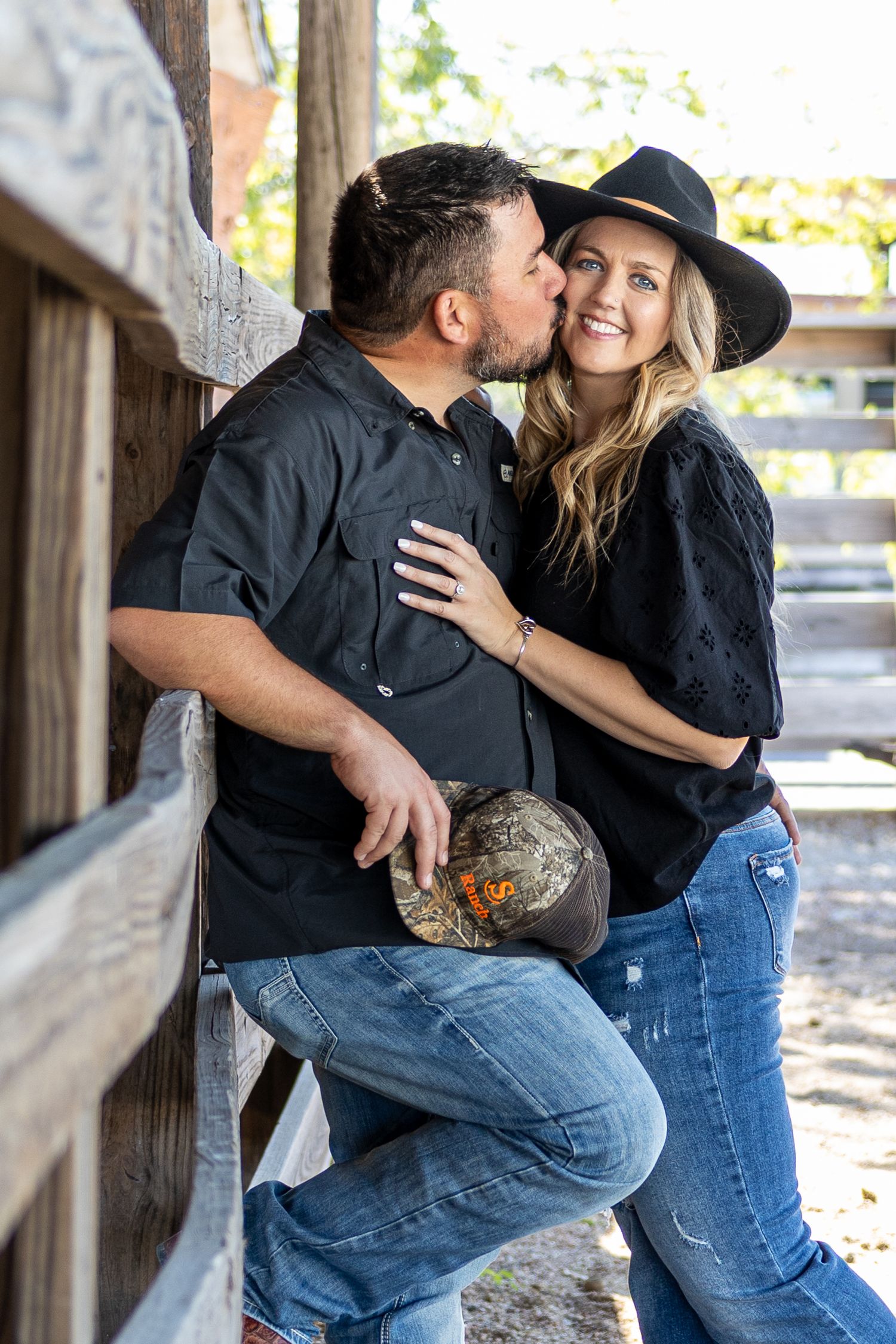 A couple in casual attire shares romantic moments against a rustic wooden backdrop.