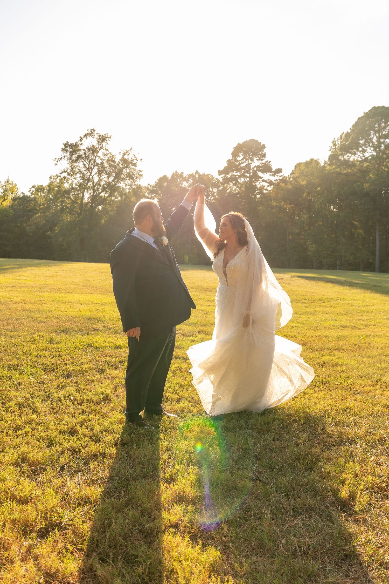 Newlyweds walk hand in hand across a sun-drenched meadow at golden hour.