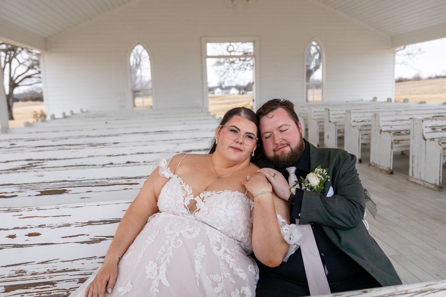 Wedding couple poses in a bright white hallway with wooden benches.