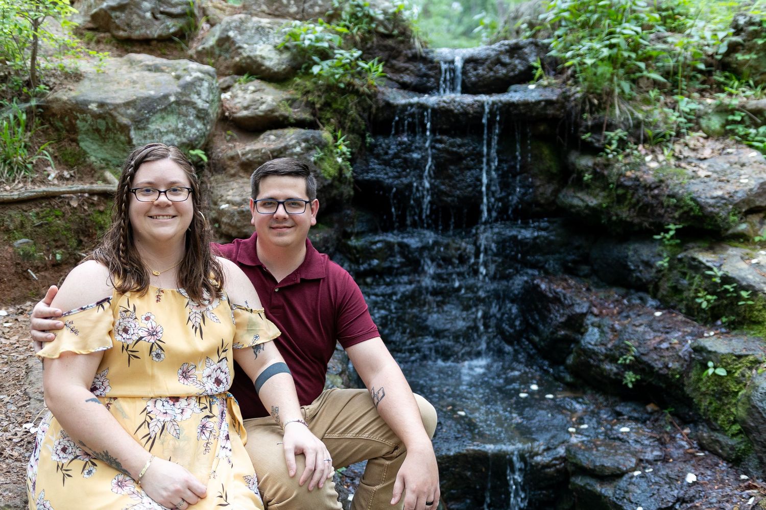 A couple shares a happy moment near a cascading waterfall in the woods.