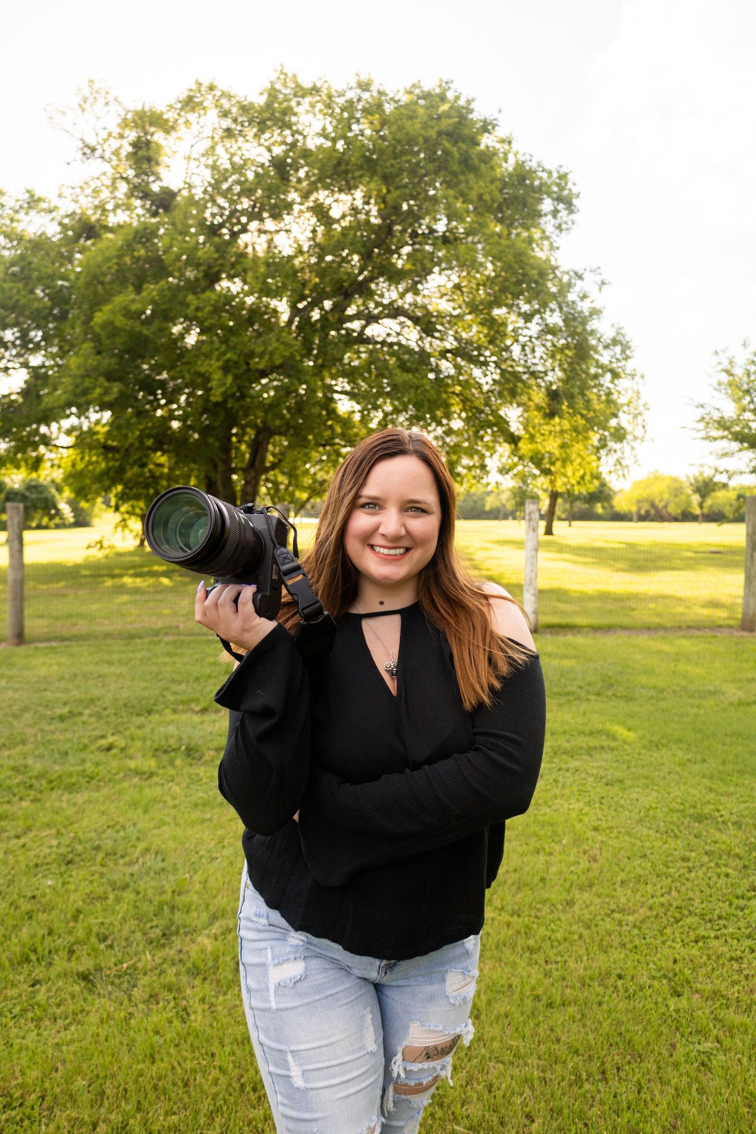 Professional photographer with cameras taking outdoor photos in sunny field.