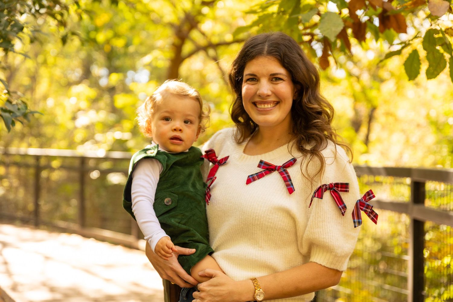 Family portrait session on wooden walkway with autumn trees and golden sunlight.