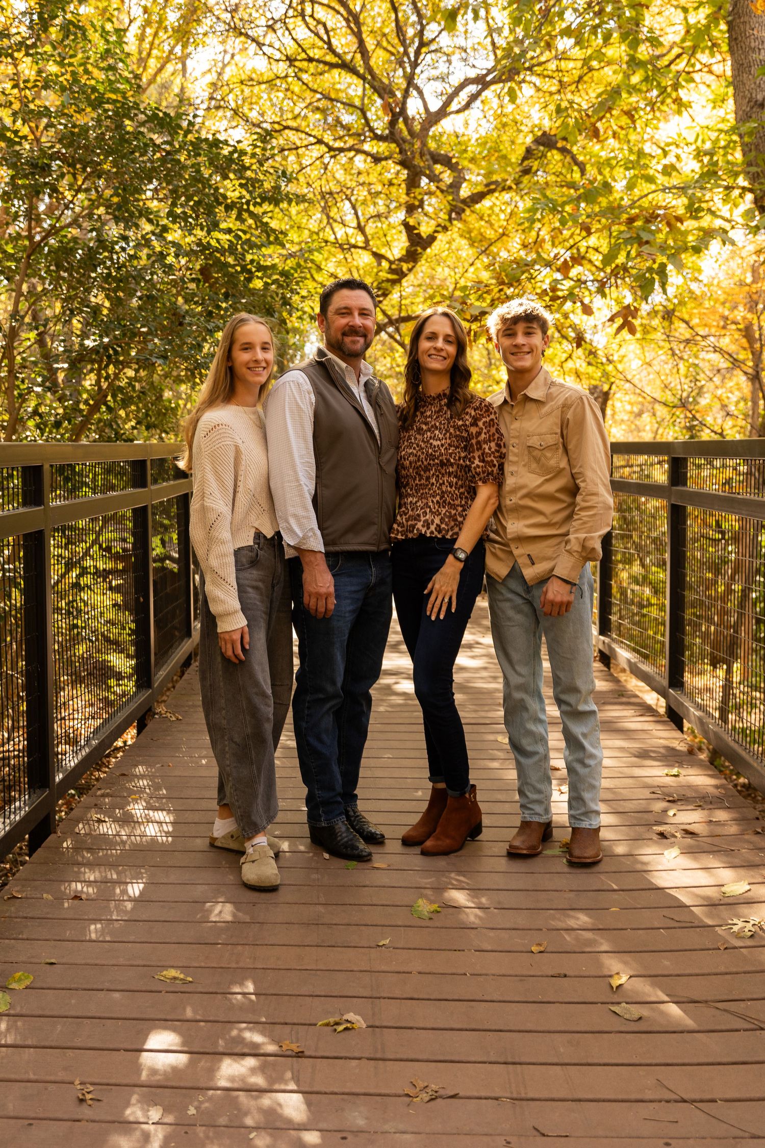 Group poses casually on wooden boardwalk with autumn trees creating a golden backdrop.