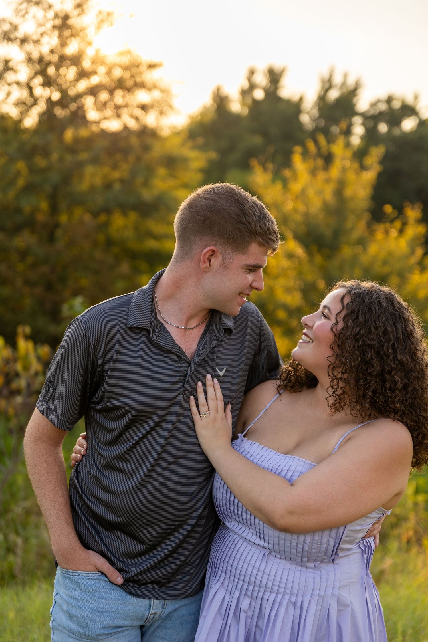 A couple shares a loving moment while standing in a field at sunset.