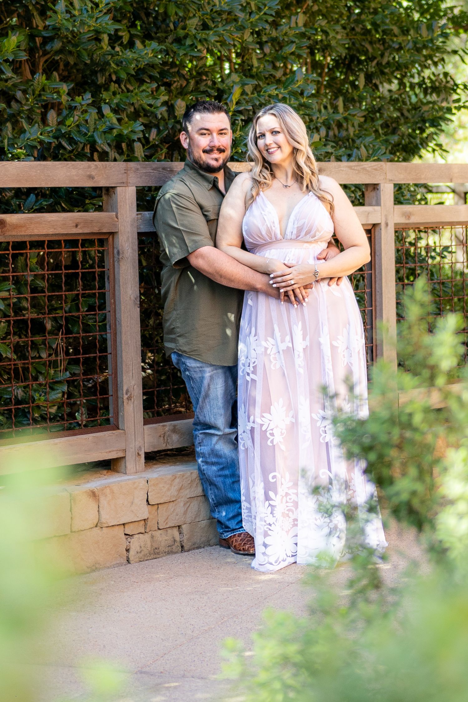 A couple embraces on a wooden deck surrounded by greenery during their engagement photoshoot.