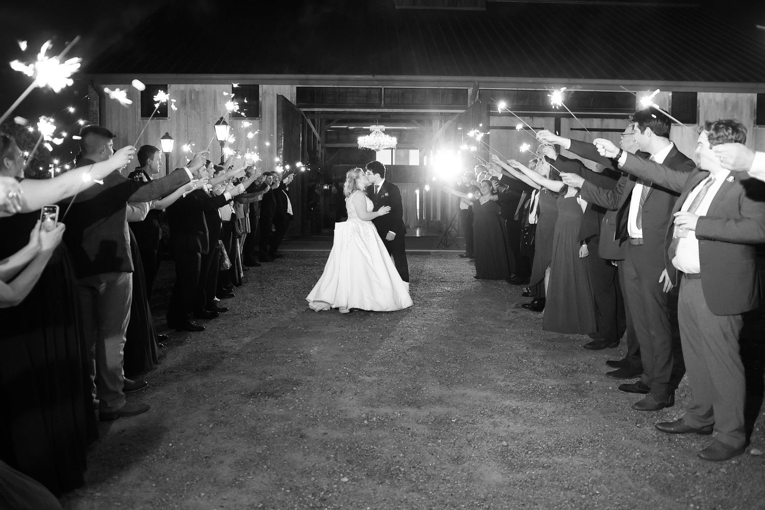 Black and white nighttime wedding exit with guests holding sparklers creating a glowing tunnel.
