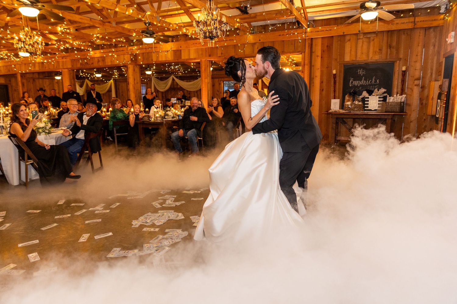Wedding reception first dance in rustic wooden venue with dramatic lighting and fog effects.
