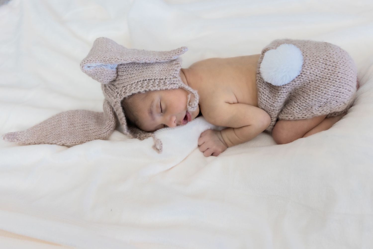 Newborn baby sleeping peacefully on soft white blankets in a series of gentle poses.