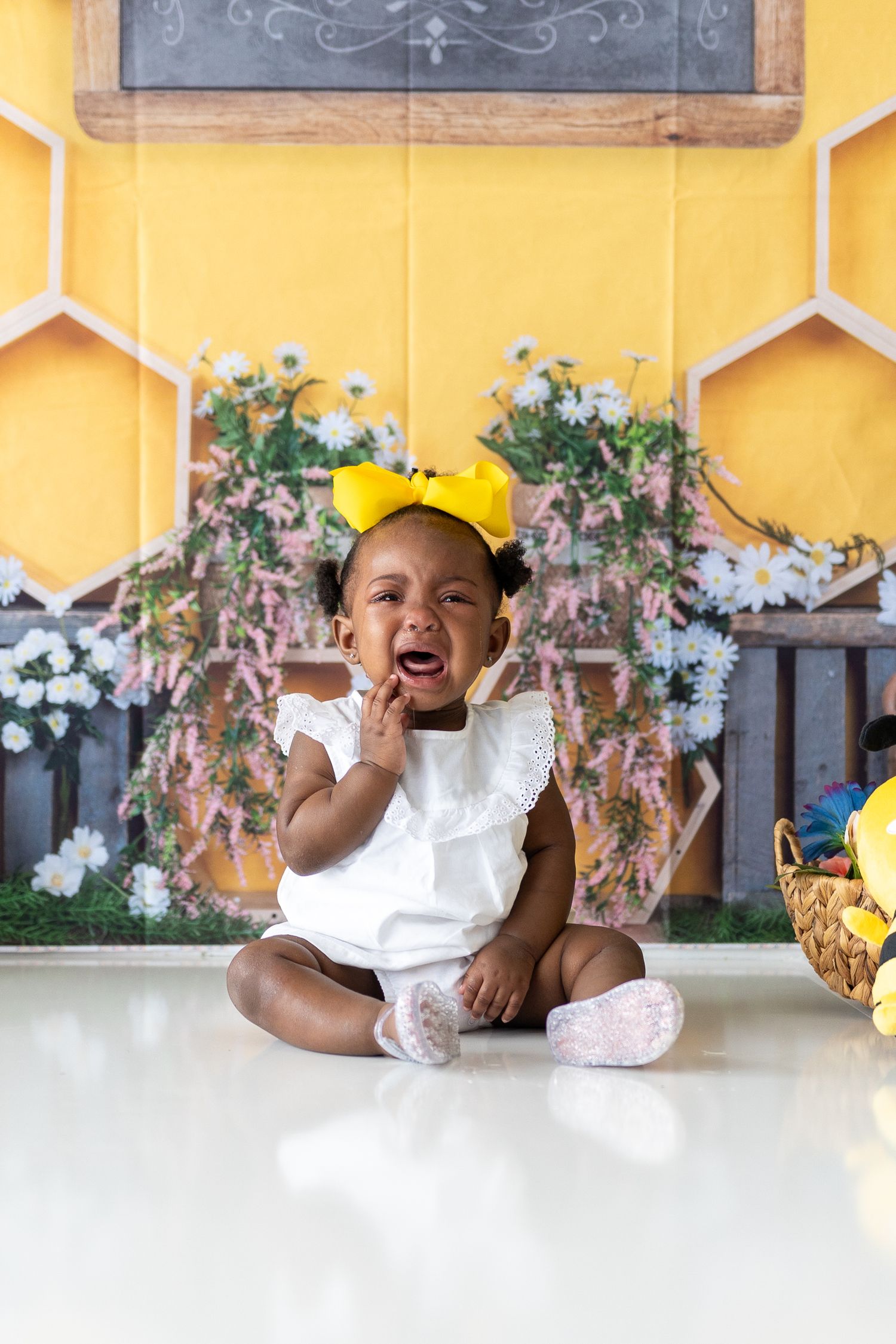 Baby photo session against yellow wall with honeycomb decorations and floral accents.