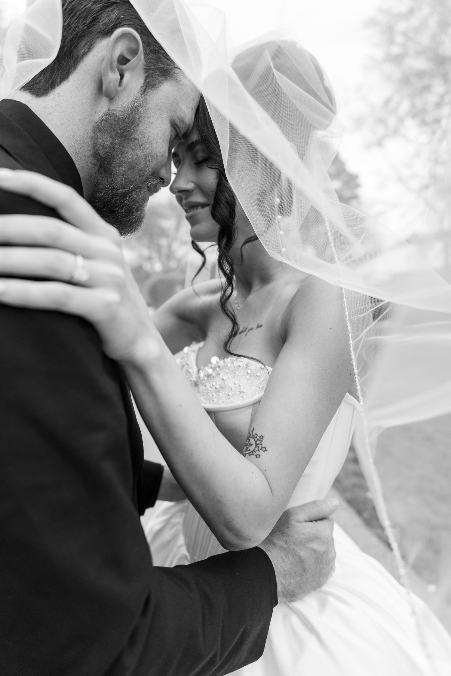 Black and white wedding portraits capture tender moments between newlyweds under a delicate veil.