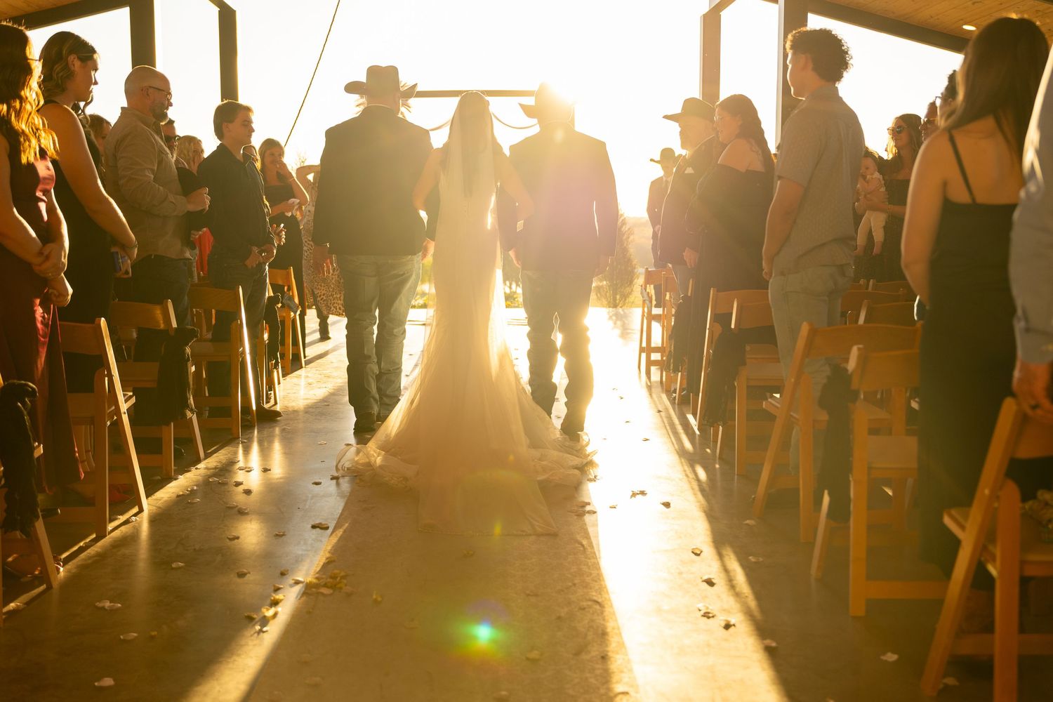 Wedding guests silhouetted against a golden sunset during an outdoor reception.