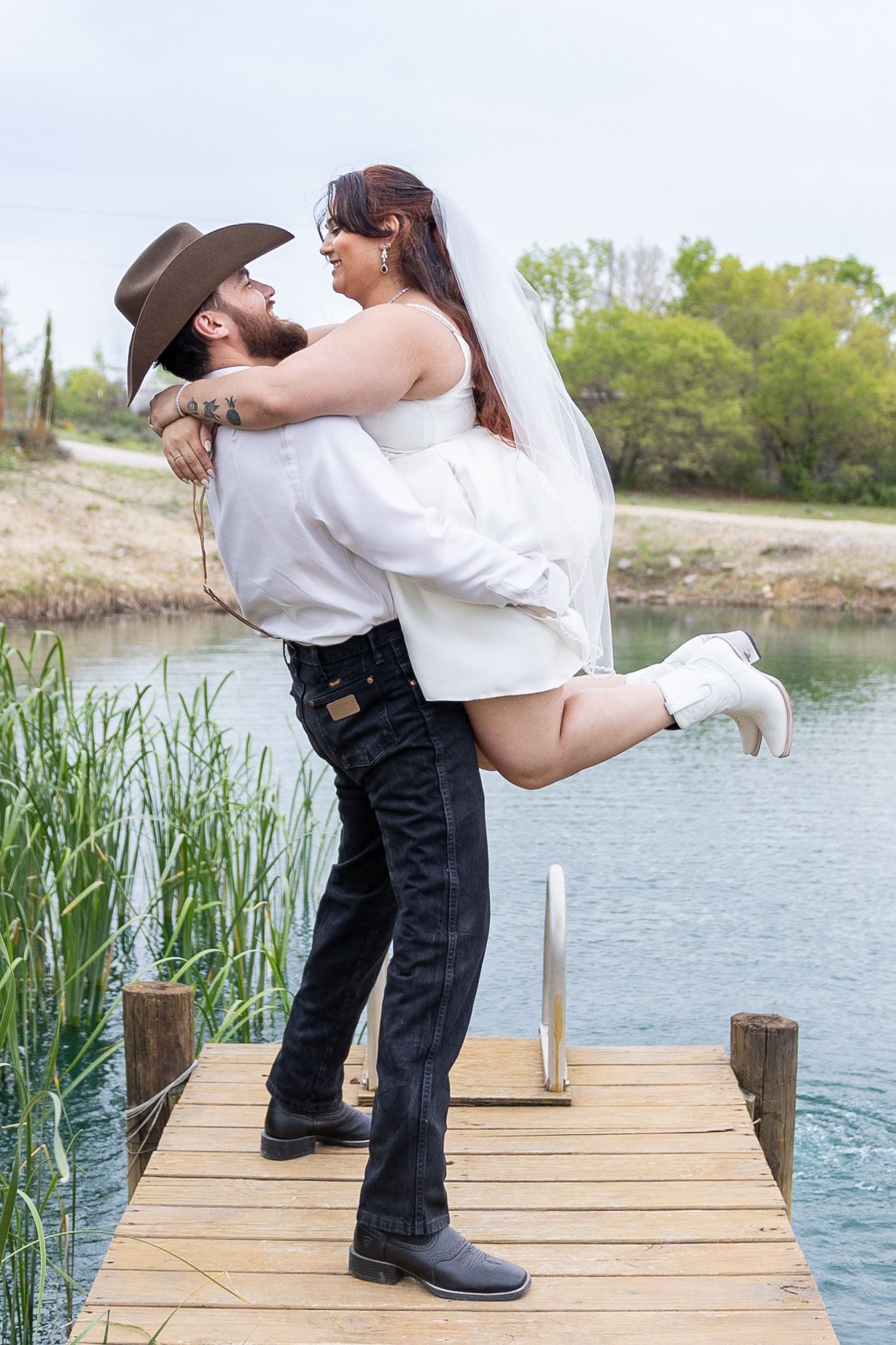 A playful wedding moment captured on a wooden dock by a serene lake.