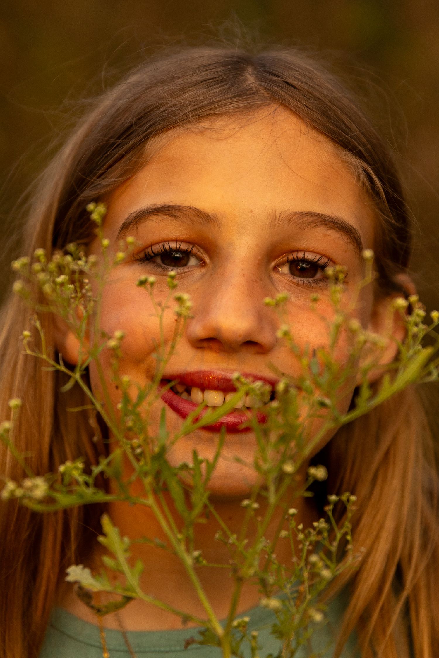 A close-up portrait through delicate wildflowers in warm golden light.