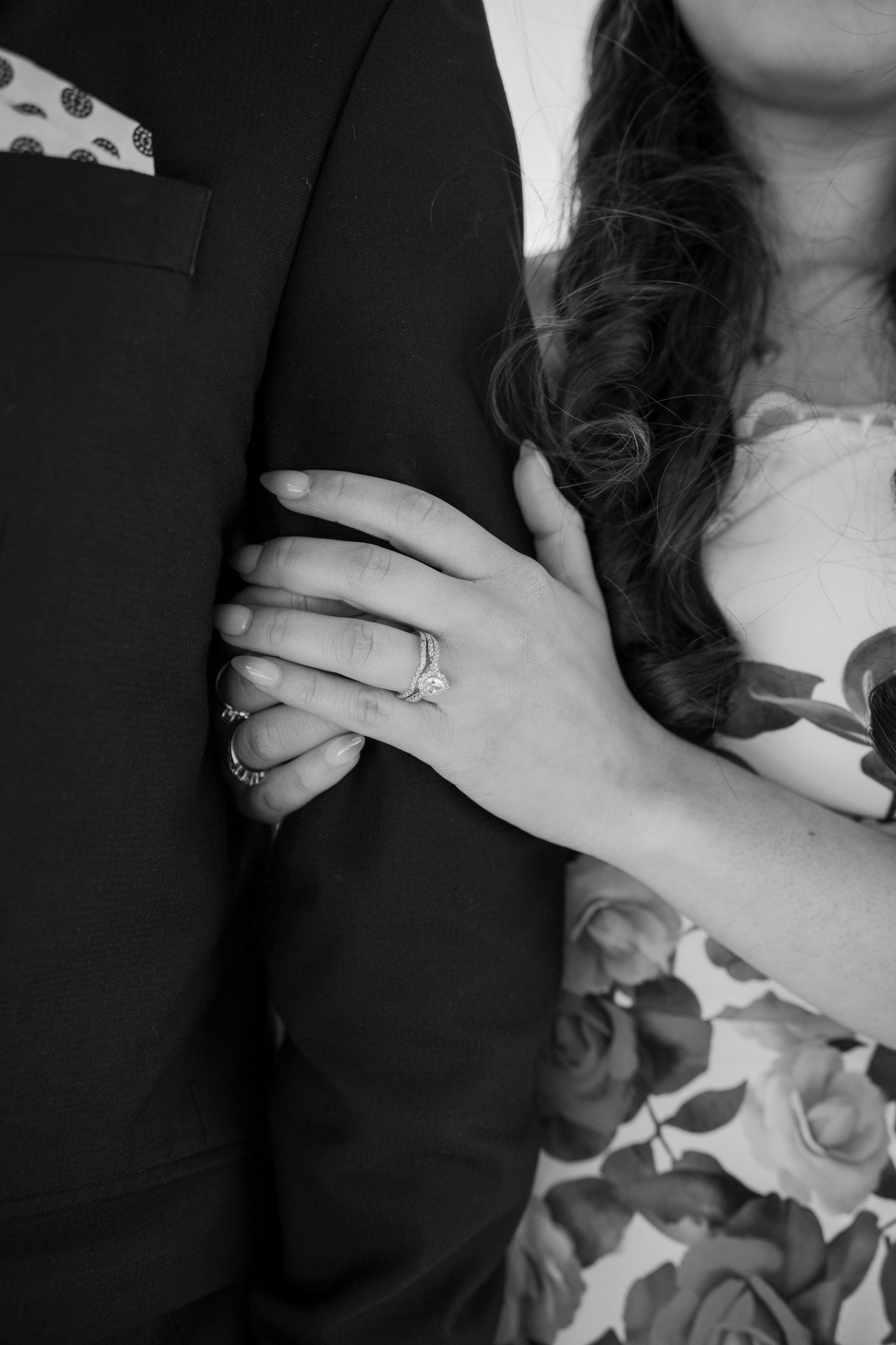 Close-up of hands showing engagement rings against formal attire with floral details.