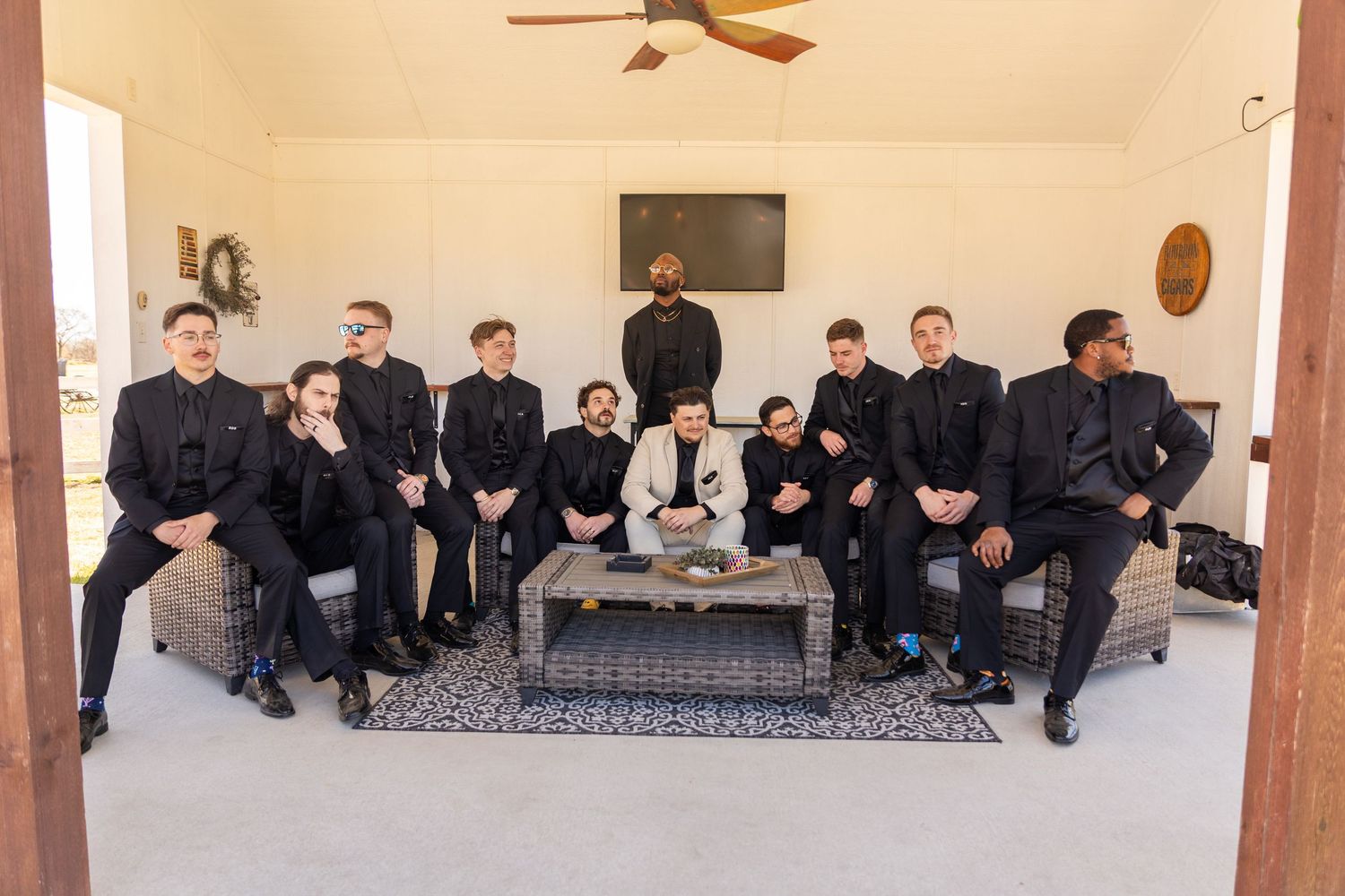 Wedding party dressed in formal attire seated along covered outdoor porch.