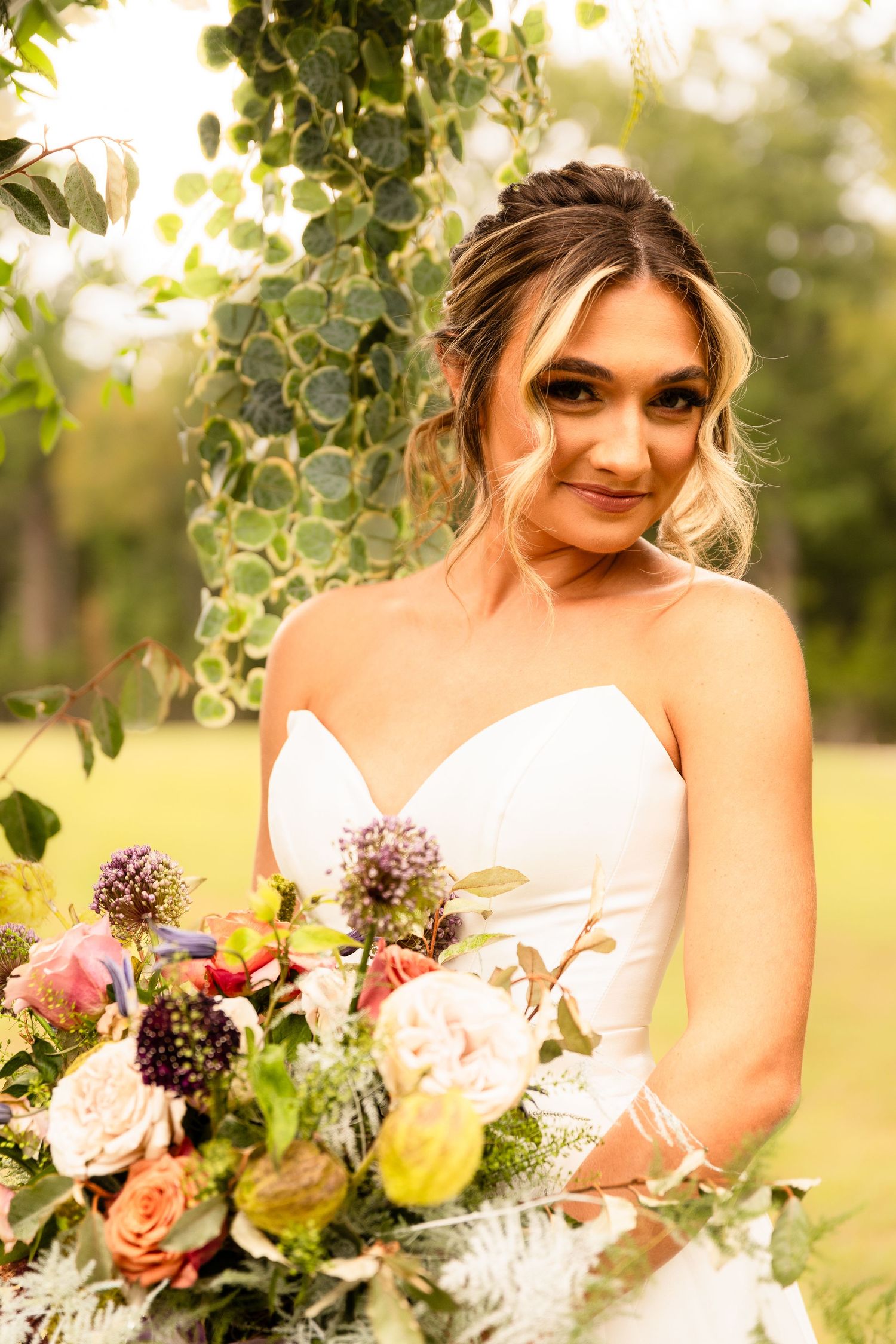 Bride holding colorful bouquet poses outdoors with natural foliage backdrop.