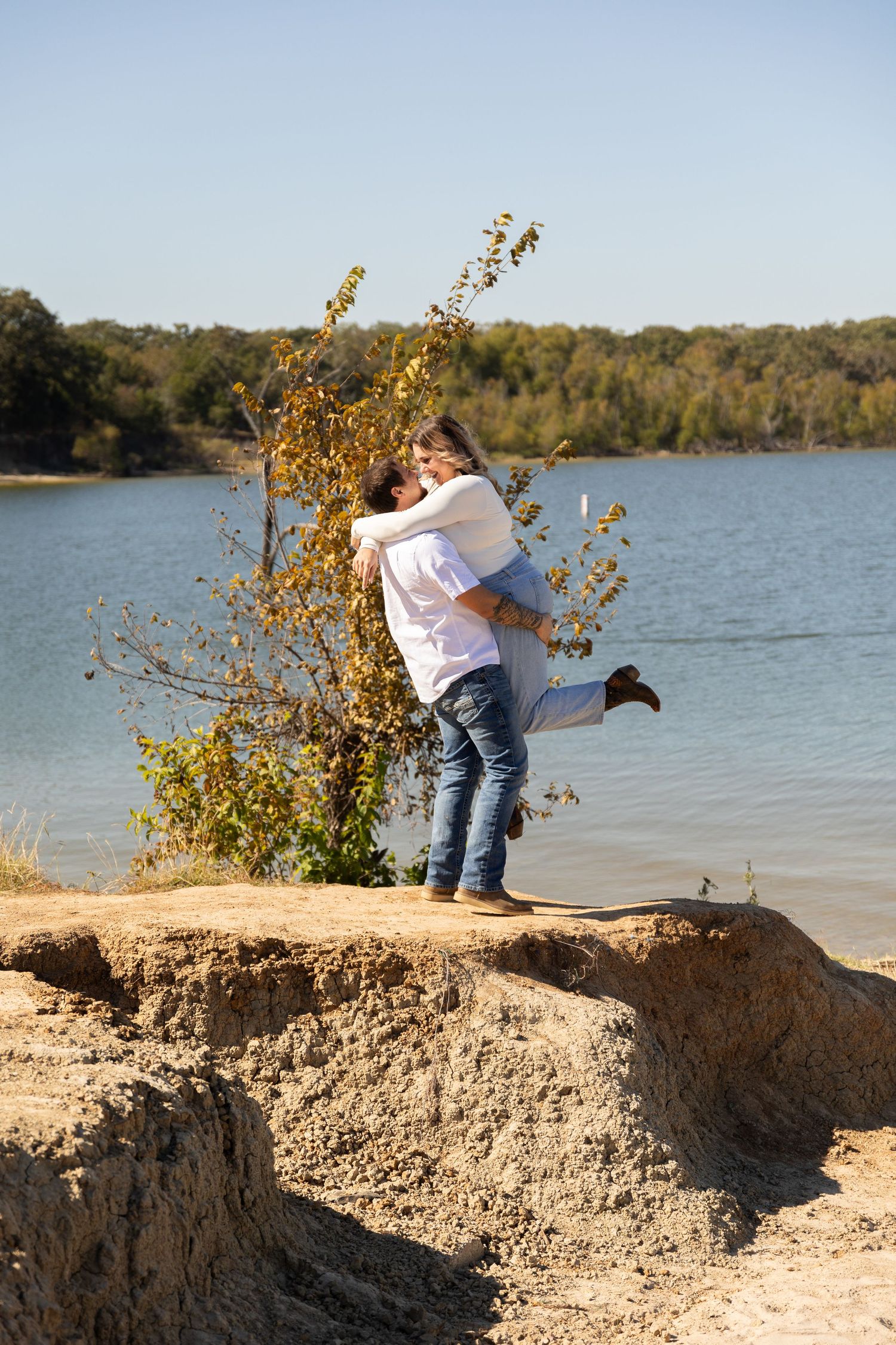 Playful couple posing and embracing on rocky cliff overlooking a serene lake.
