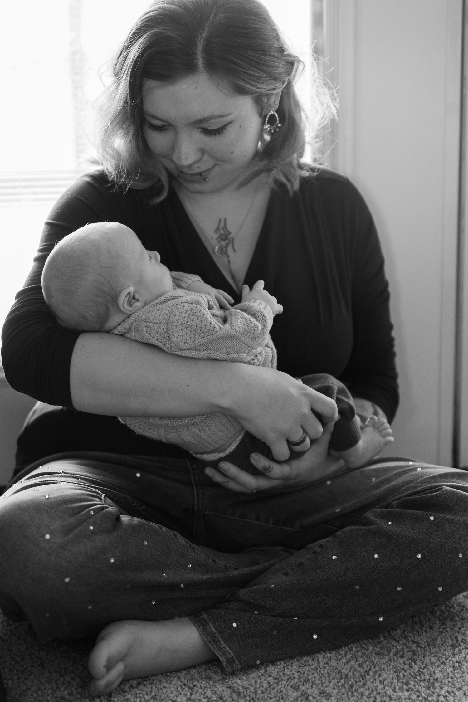 Black and white portrait of parent cradling newborn baby in peaceful indoor setting.