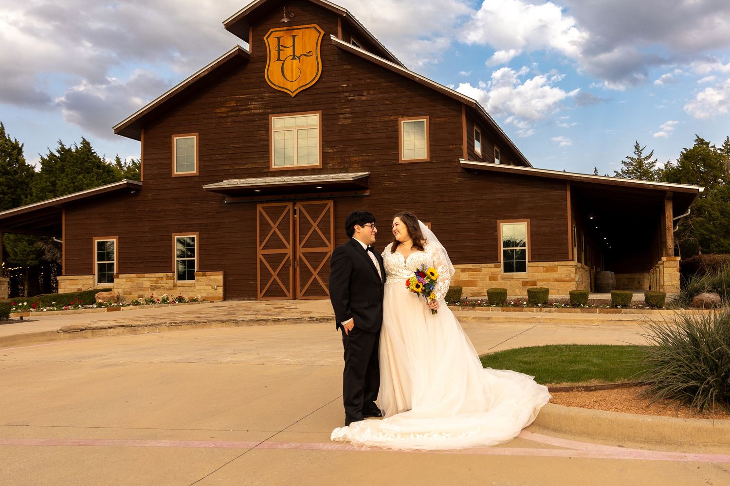 Rustic brown barn wedding venue with elegant white decorations against a cloudy sky.