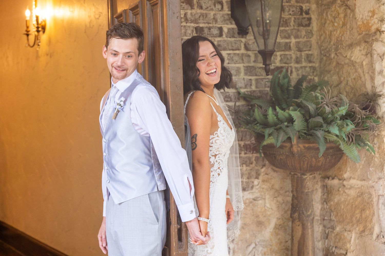Wedding couple posing playfully against a rustic brick wall with warm lighting.