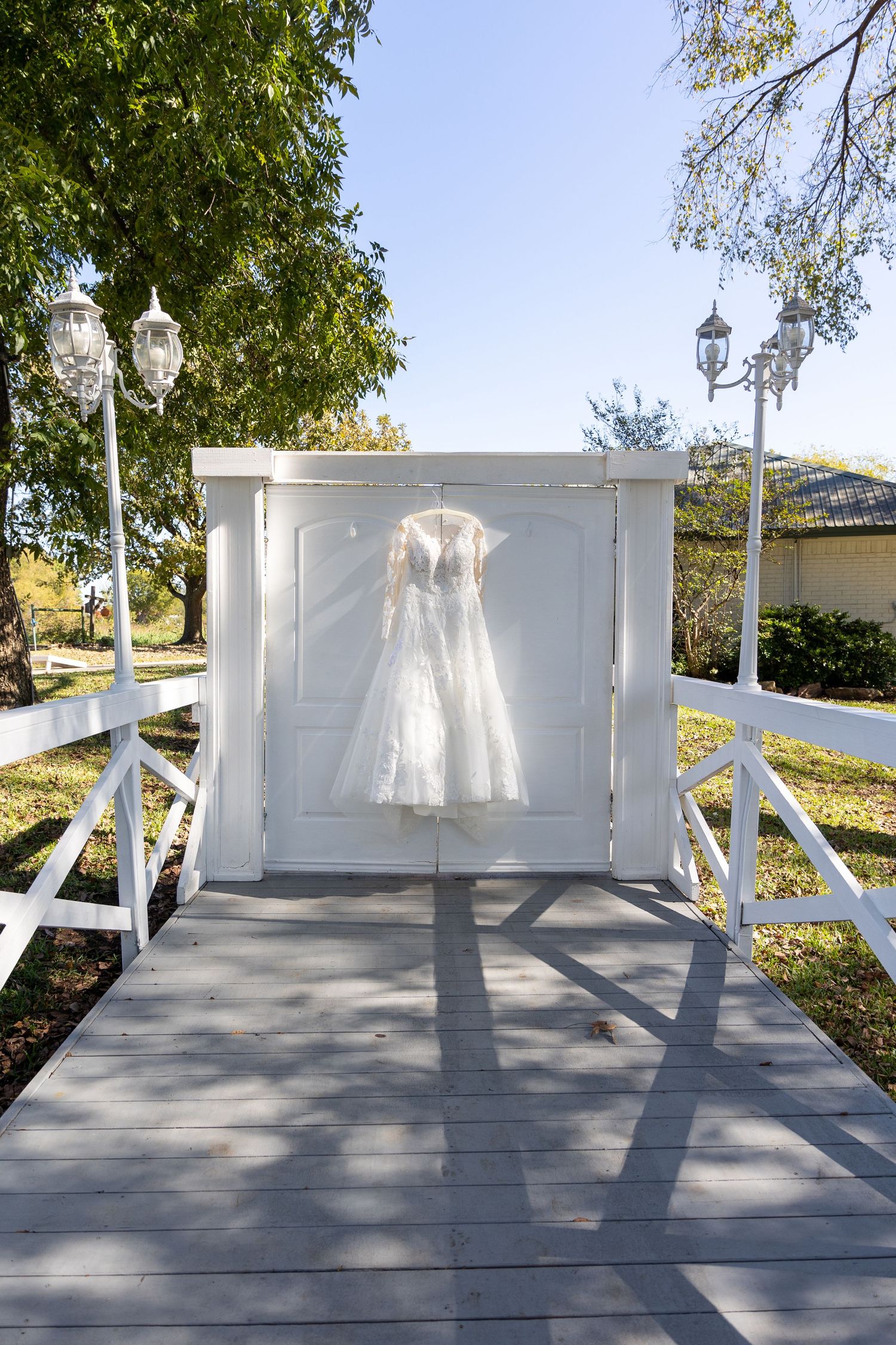 White wedding dress displayed on outdoor white wooden gazebo in natural sunlight.
