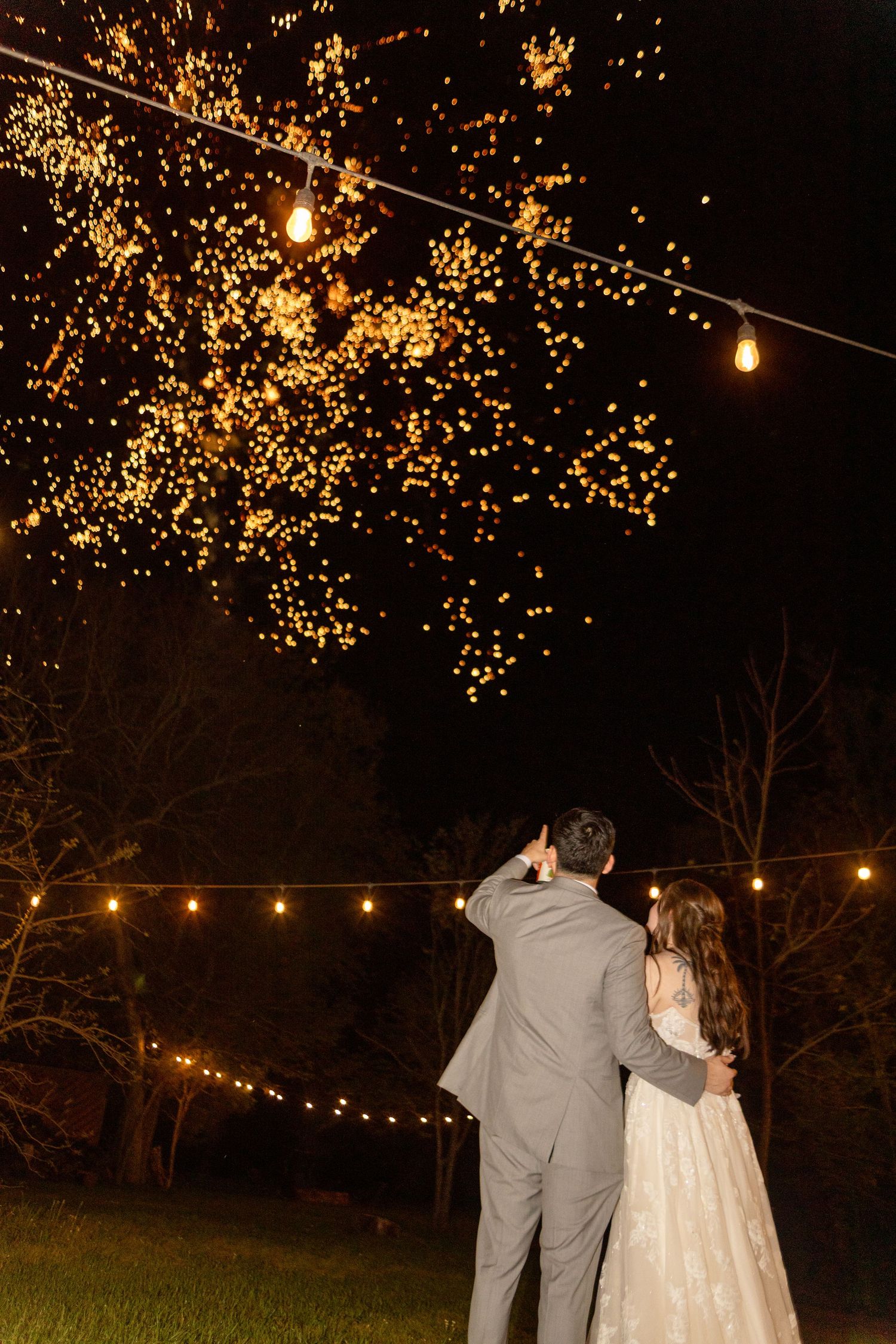 Newlyweds gaze at string lights and illuminated trees during their evening reception.