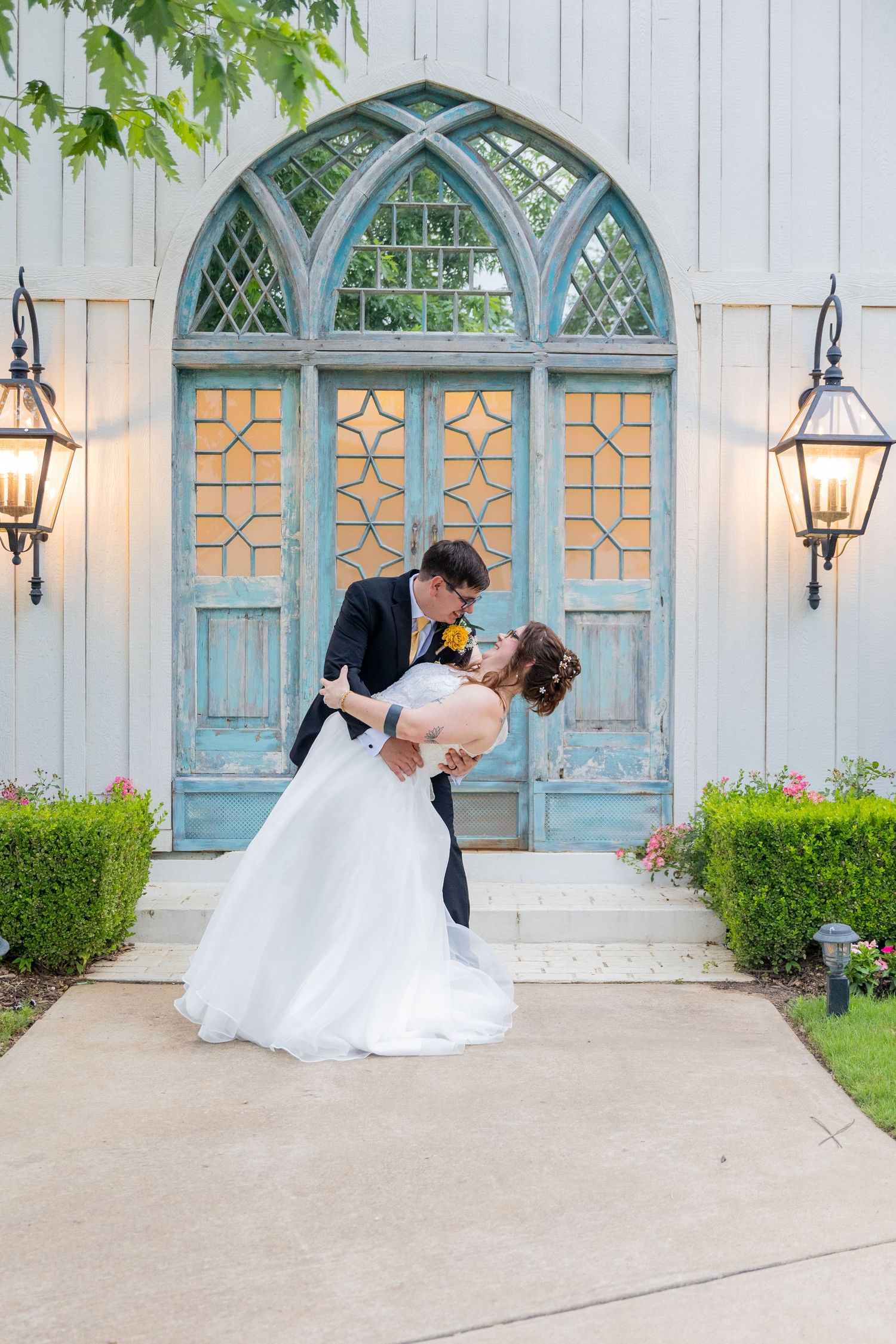 Romantic wedding scene in front of vintage blue chapel doors with gas lanterns.