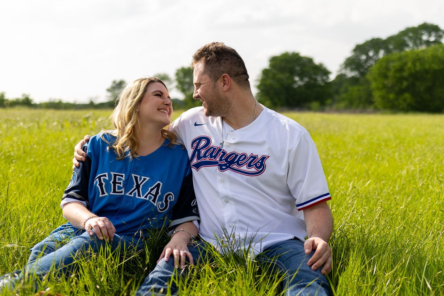 A couple shares a romantic moment while sitting in a grassy field on a sunny day.