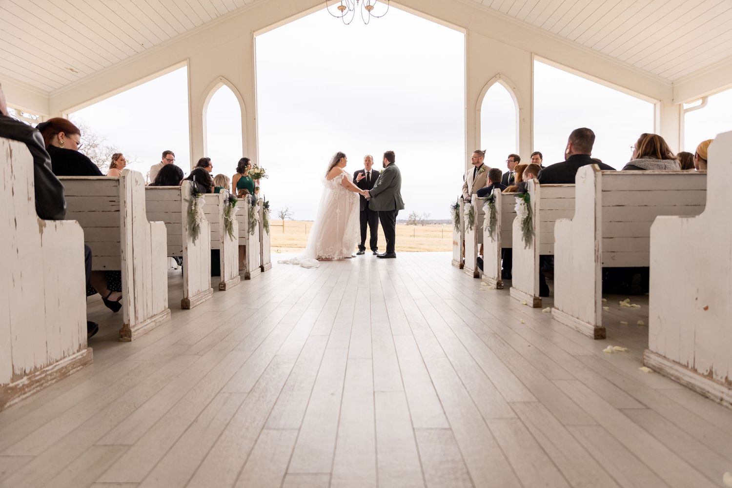White chapel interior with wooden pews and guests seated for a wedding ceremony.