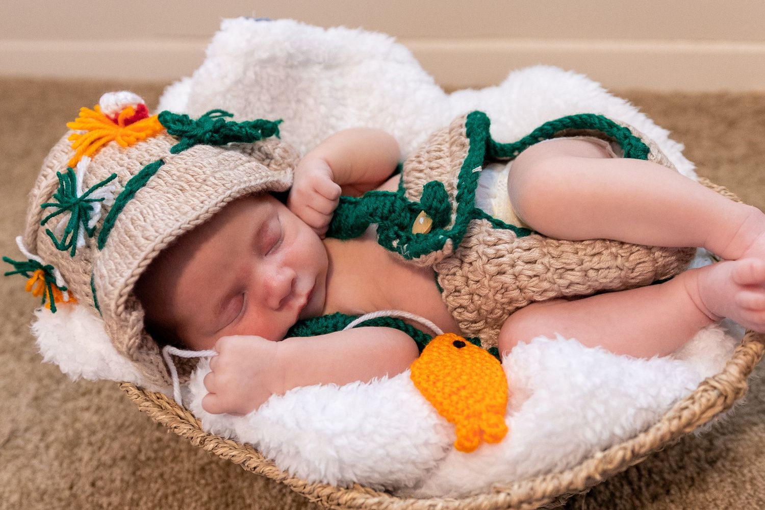 Sleeping baby in crochet outfit with orange accents lying on white blanket.