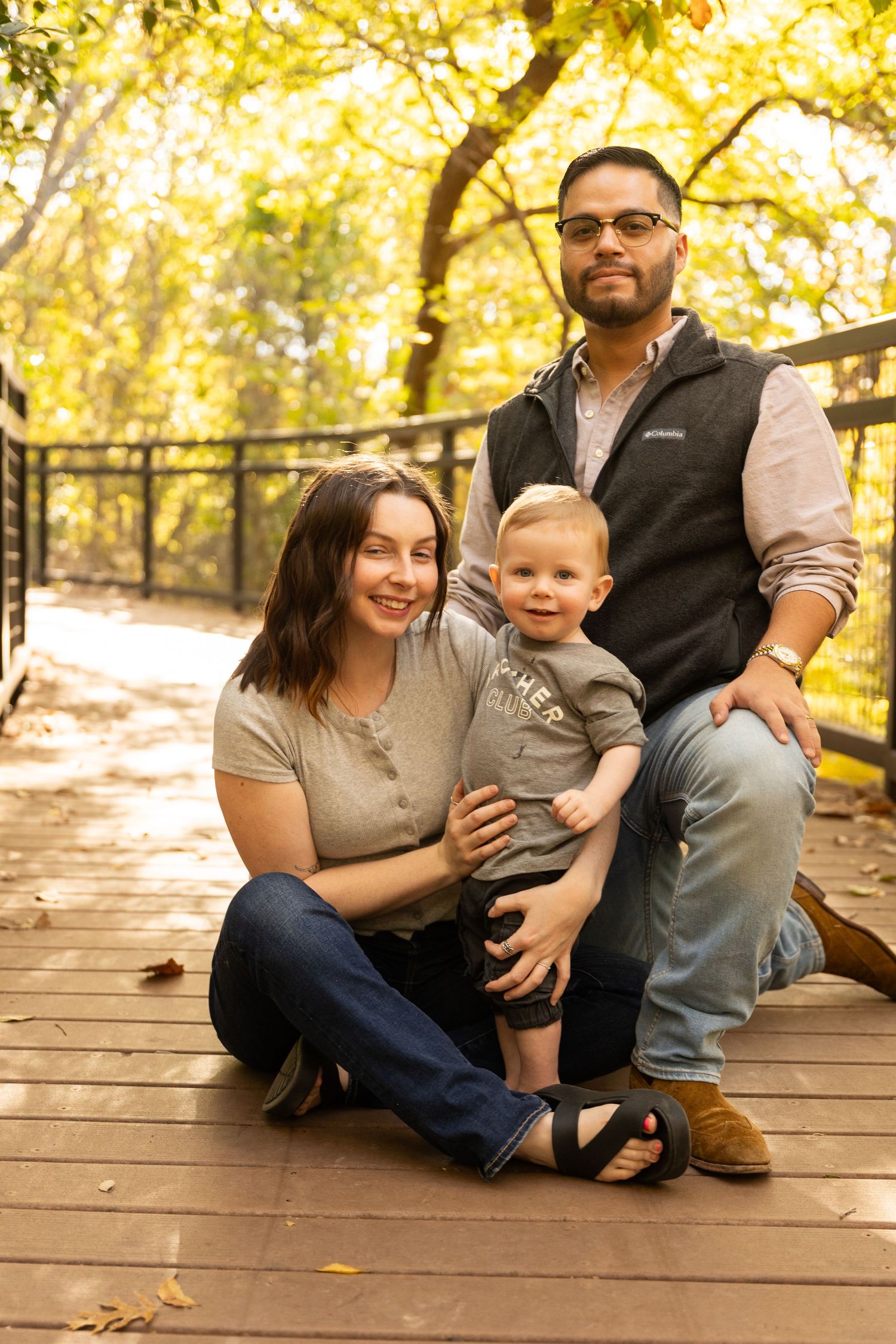 Family sitting together on wooden deck with warm sunlight filtering through fall trees.