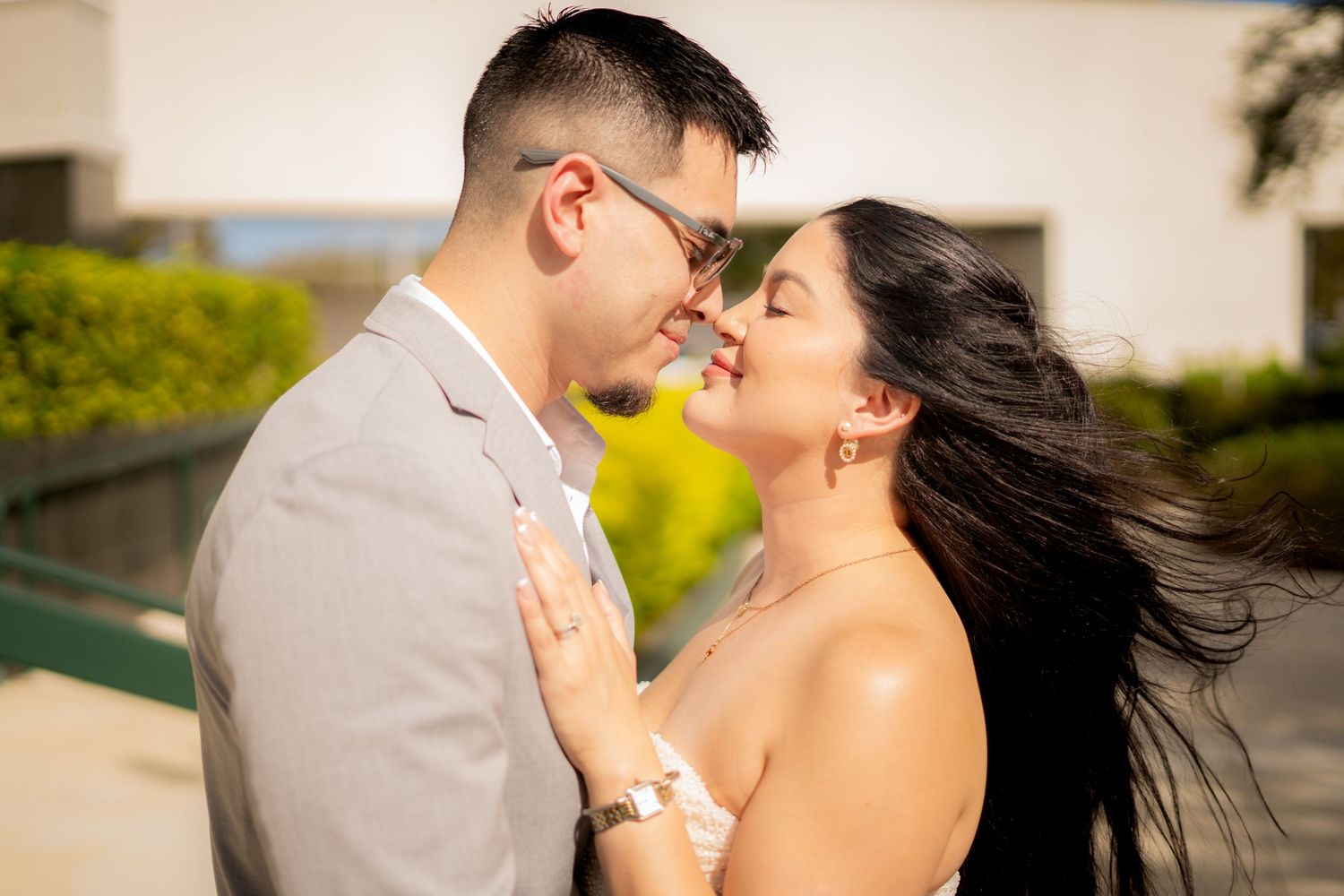 Couple smiling and nearly kissing outdoors with wind blowing hair.