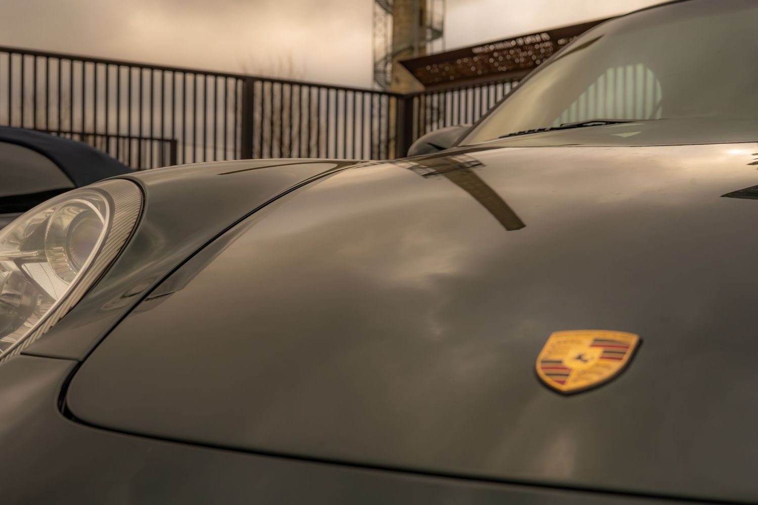 Close-up of gray Porsche hood featuring iconic gold Porsche crest emblem badge.