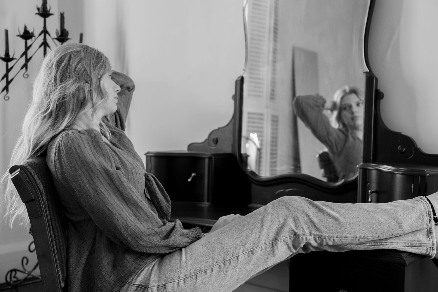 Black and white portrait of blonde woman sitting at vintage vanity mirror.