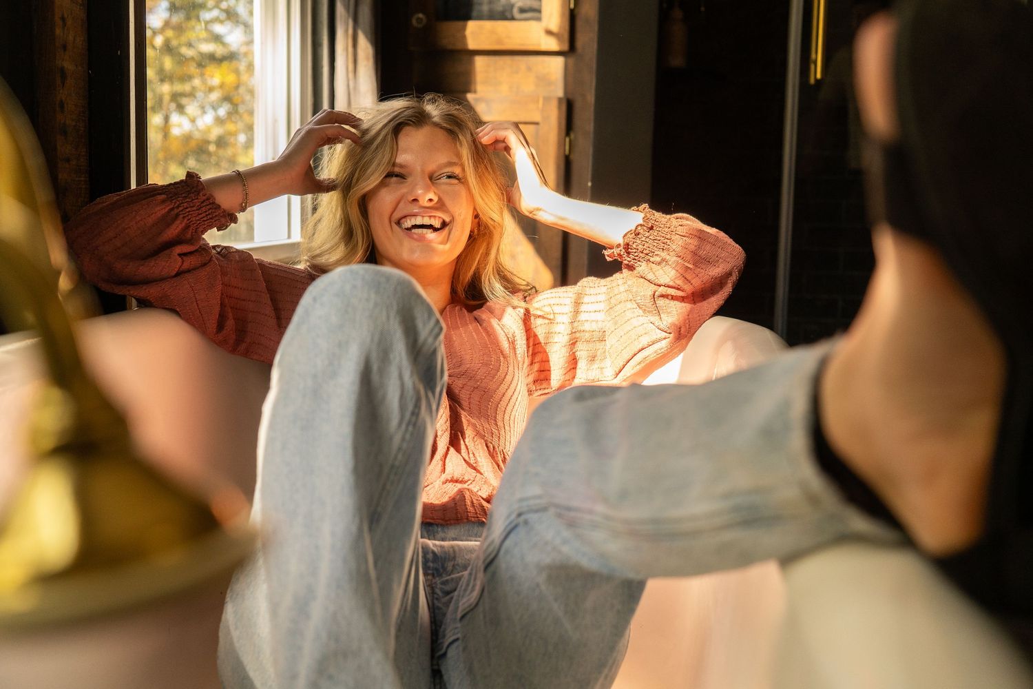 Laughing blonde woman sitting in warm sunlight with friends in cozy room.