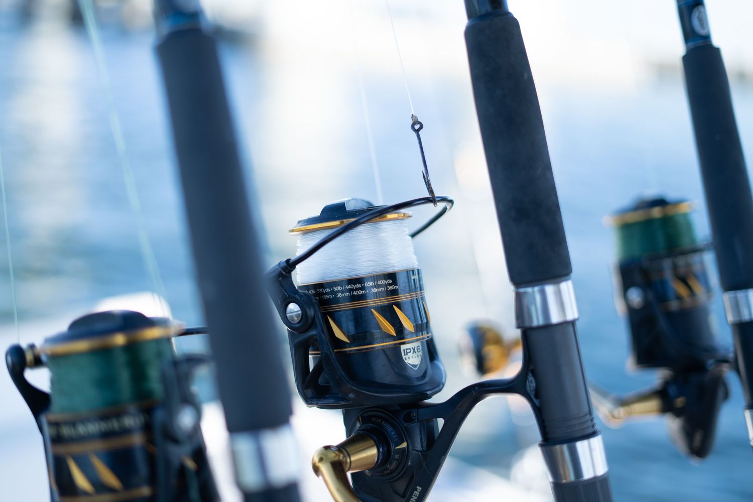 Close-up of spinning fishing reels on rods against a bright blue water background.