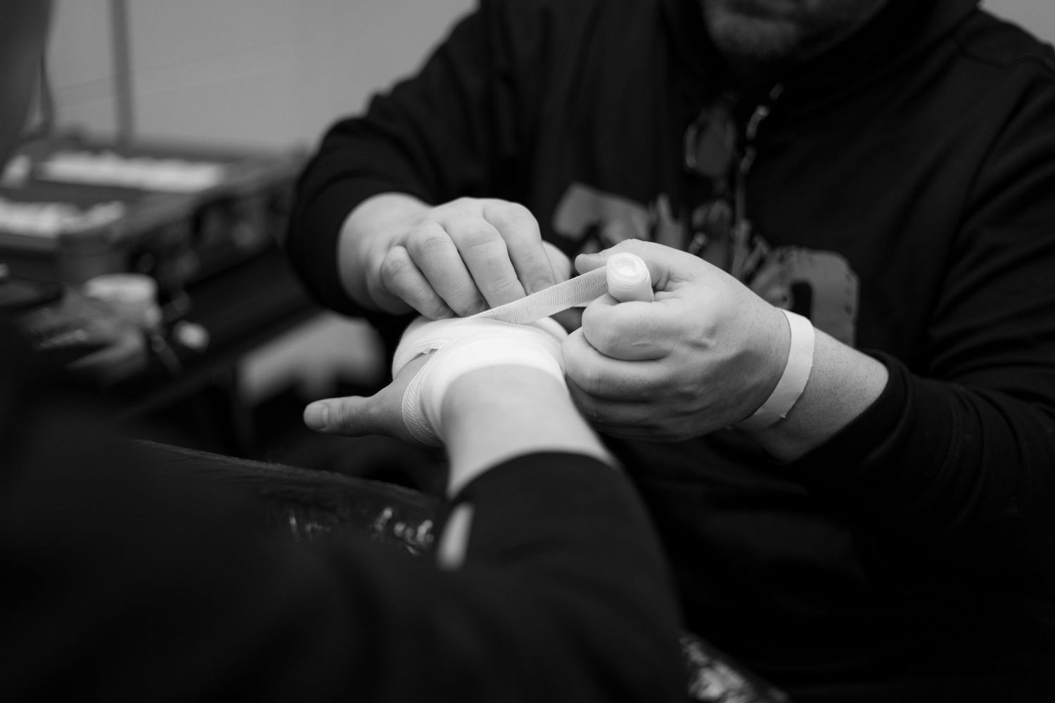 Black and white close-up of hands wrapping a boxer's wrists before a fight.
