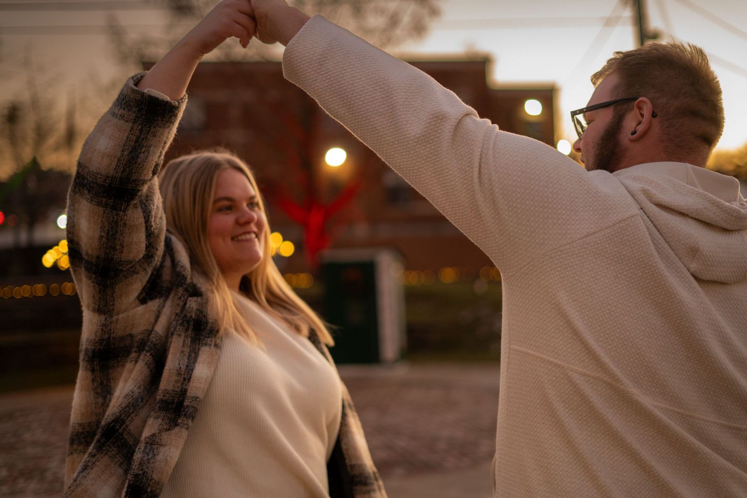 Couple dancing outdoors at dusk with festive string lights in background.