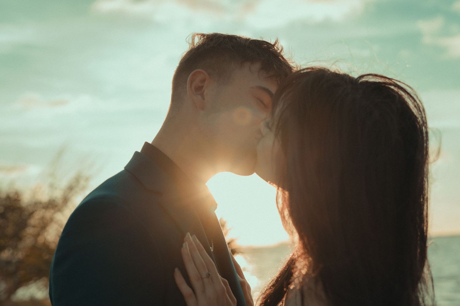 Romantic couple kissing at sunset with golden backlight by the sea.