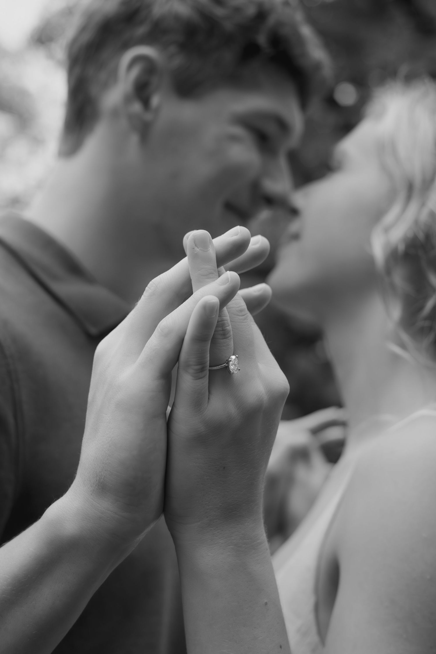 Black and white photo of hands clasped together with an engagement ring.
